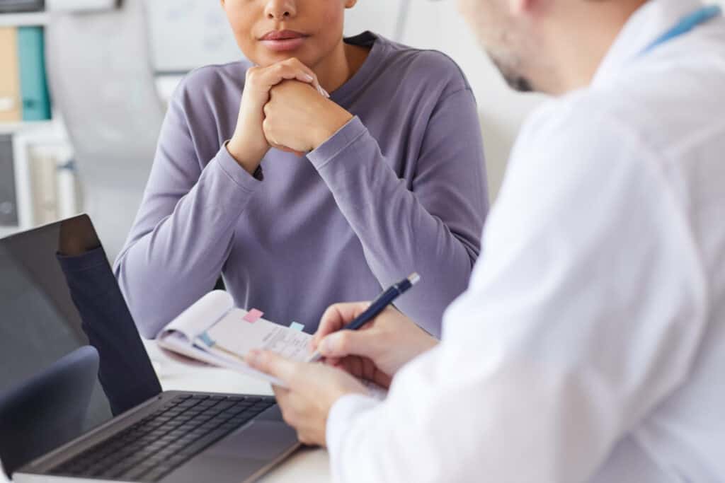 Close-up of male doctor writing a prescription to his patient at the table at hospital